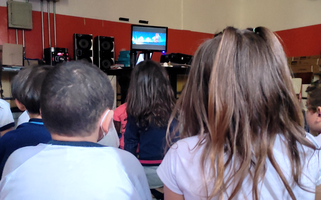 Crianças em uma sala de vídeo sentadas assistindo a um vídeo de animação.